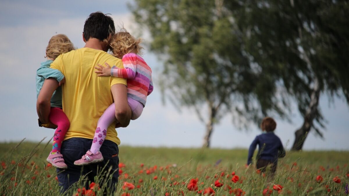 man carrying to girls on field of red petaled flower