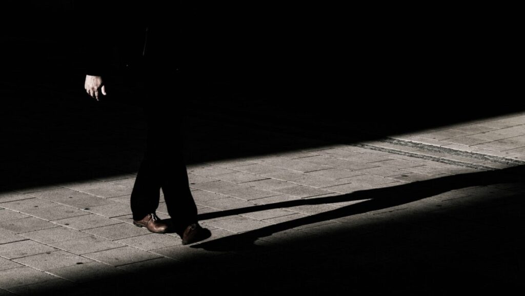 person walking on narrow pathway with shadow on gray floor