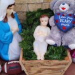 Boy gifts baby Jesus with football, teddy bear at Nativity